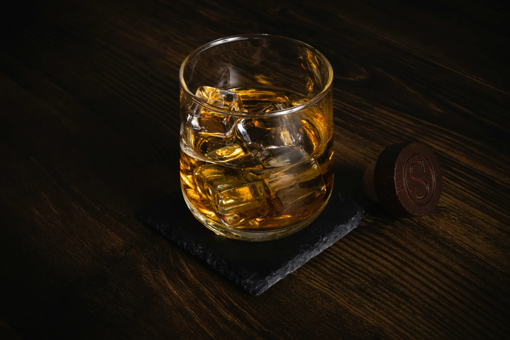 Glas whisky med is på ett mörkt träbord